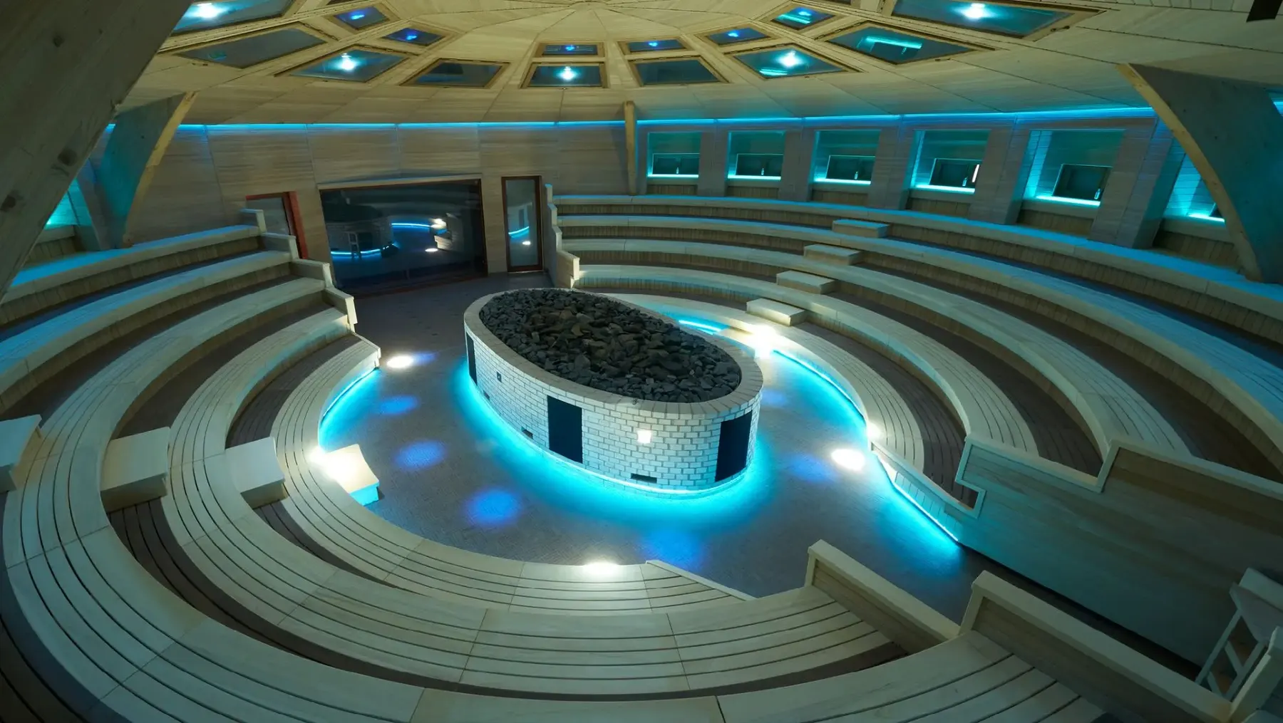 The Aquardens sauna theatre in Italy, lit in deep blue around the central stove